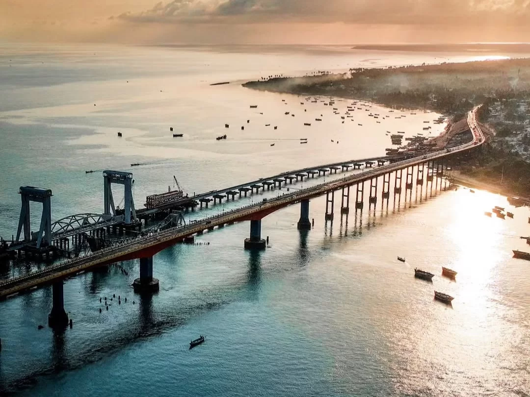 Pamban Bridge view at Pamban Beach in Rameswaram during golden hour sunset, featuring fishing boats, sea waters, reflections, perfect Rameswaram tour package.