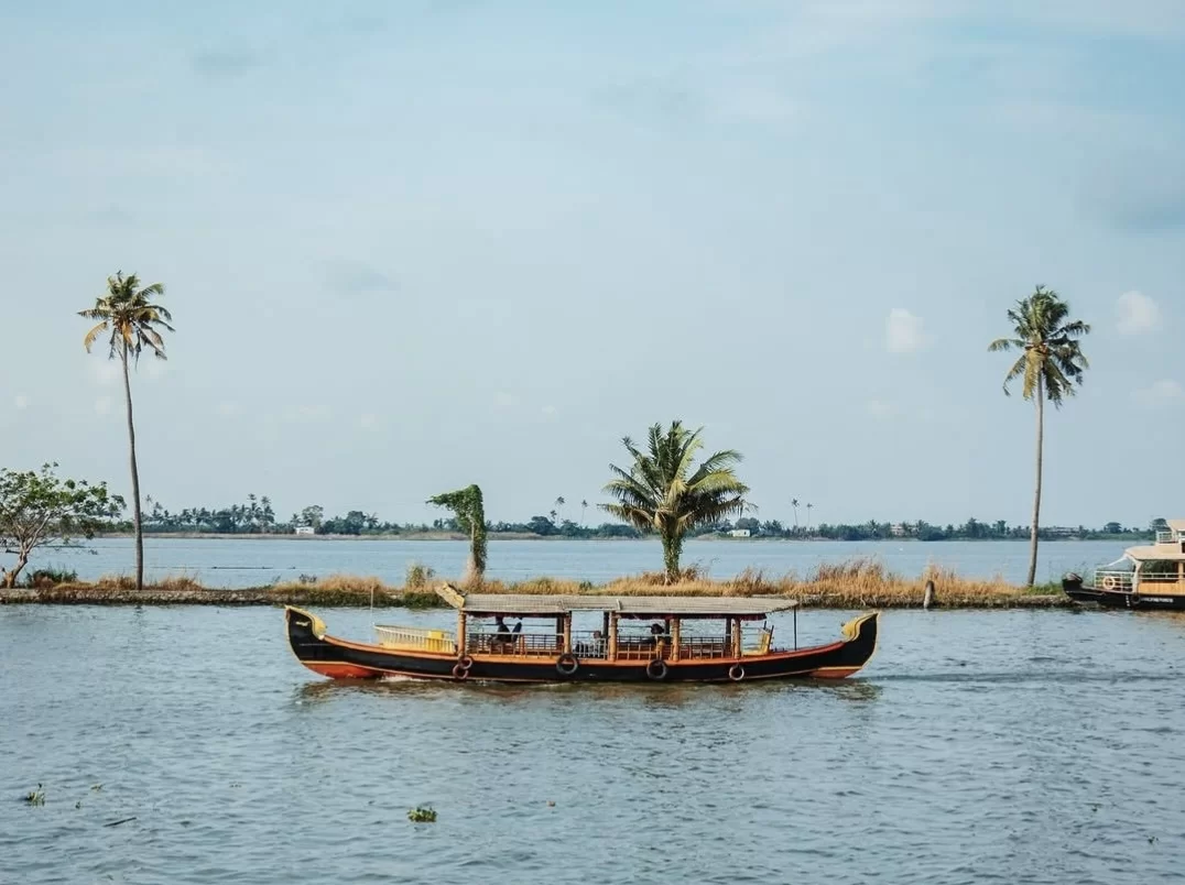 Traditional houseboat cruising at Munroe Island during partly cloudy skies, featuring palms backwaters greenery, perfect romantic Kerala tour package.