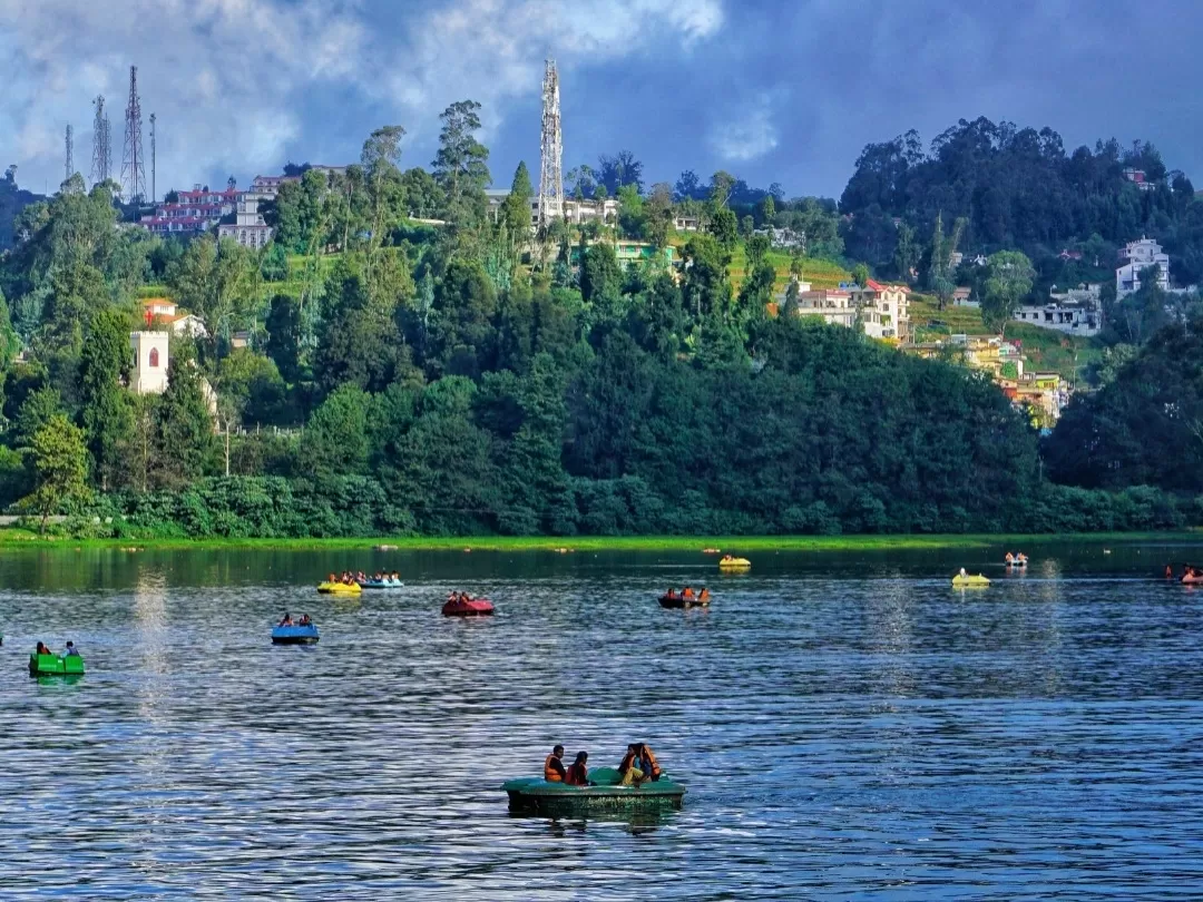 Serene Ooty Lake Udhagamandalam Nilgiris Tamil Nadu India with colorful pedal boats rowboats on calm waters eucalyptus shola forest backdrop distant church spire telecom towers misty hills colonial buildings boaters enjoying ride, perfect Nilgiri hill sta
