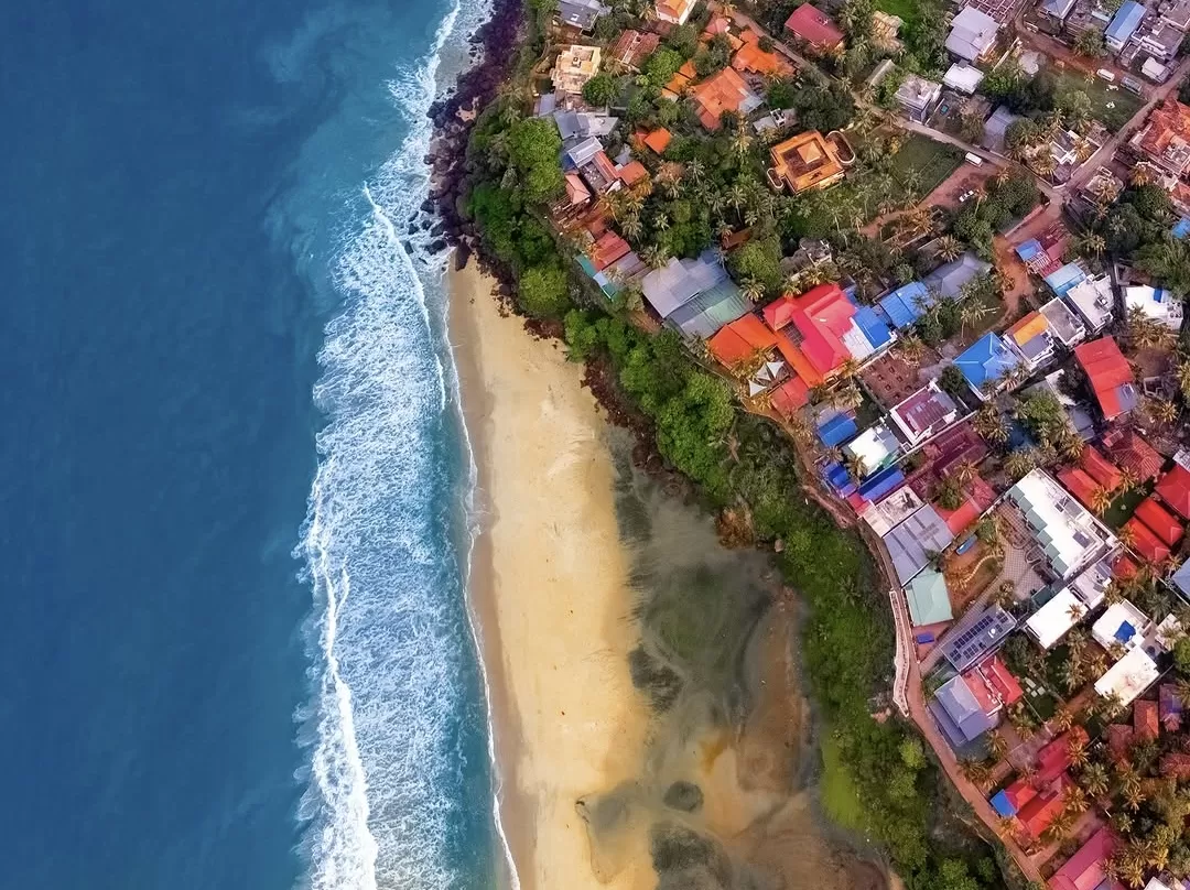 Varkala Cliff Kerala aerial colorful rooftops Arabian Sea golden beach, vibrant huts palms turquoise waves crashing rocks, perfect Kerala Papanasam Cliff village package.
