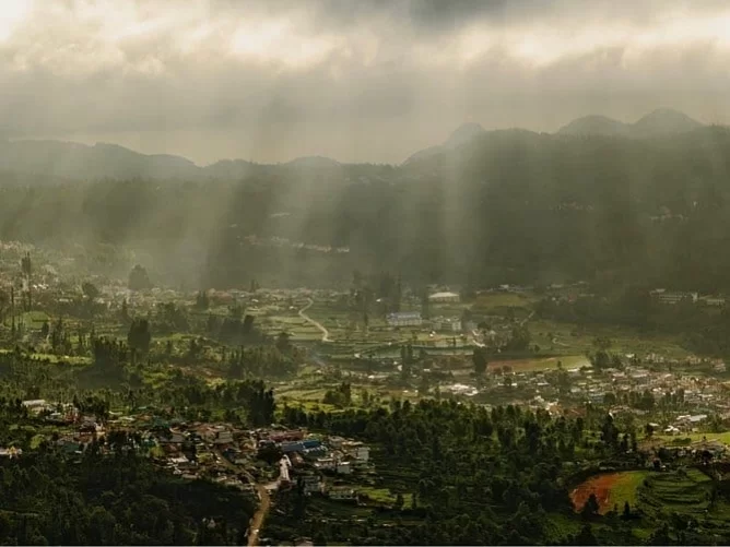 Panoramic Ketti Valley View Point Ooty Nilgiris Tamil Nadu India showcasing misty green Nilgiri hills terraced fields scattered villages winding roads sun rays piercing dramatic clouds rolling valleys, perfect Nilgiri hill station tour package