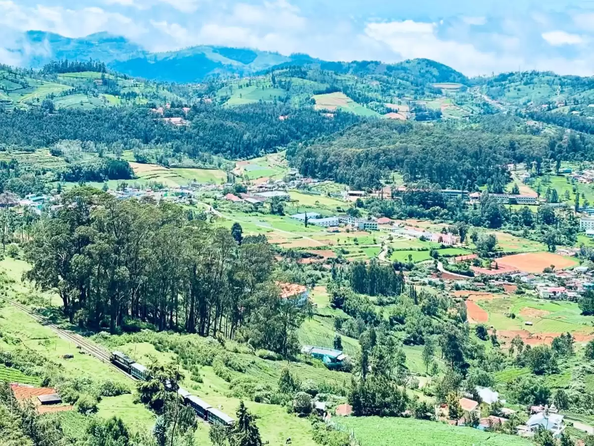 Expansive Ketti Valley View Point Ooty Nilgiris Tamil Nadu India landscape with distant blue hills partly cloudy skies lush green shola forests terraced fields colorful villages eucalyptus groves patchwork agriculture railway track, perfect Nilgiri hill s