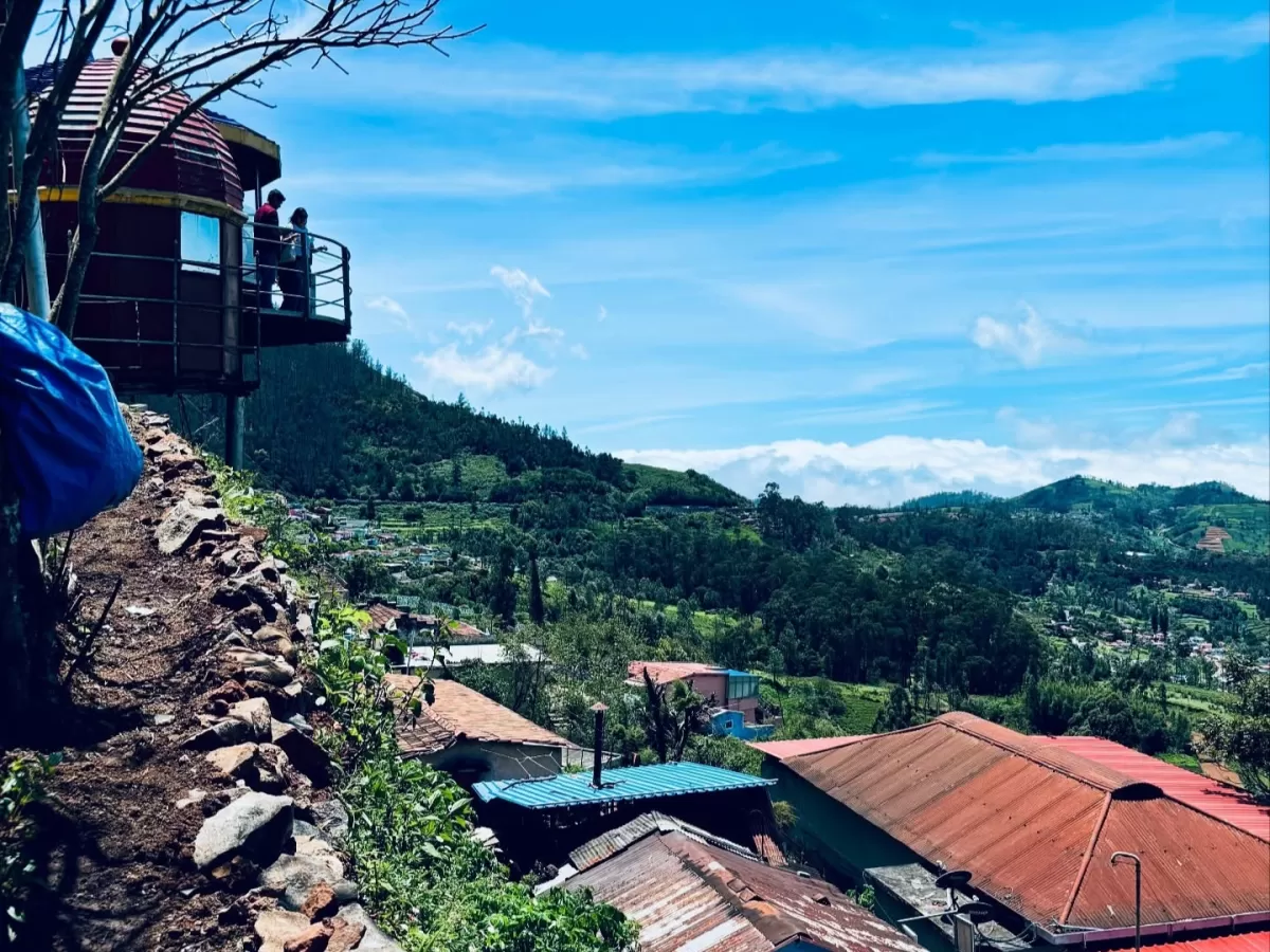 Ketti Valley View Point Ooty Nilgiris Tamil Nadu India closeup featuring maroon dome glass-walled observation deck balcony with tourists overlooking clear blue skies green hills terraced fields colorful tin roofed village homes stone walls blue tarp cover