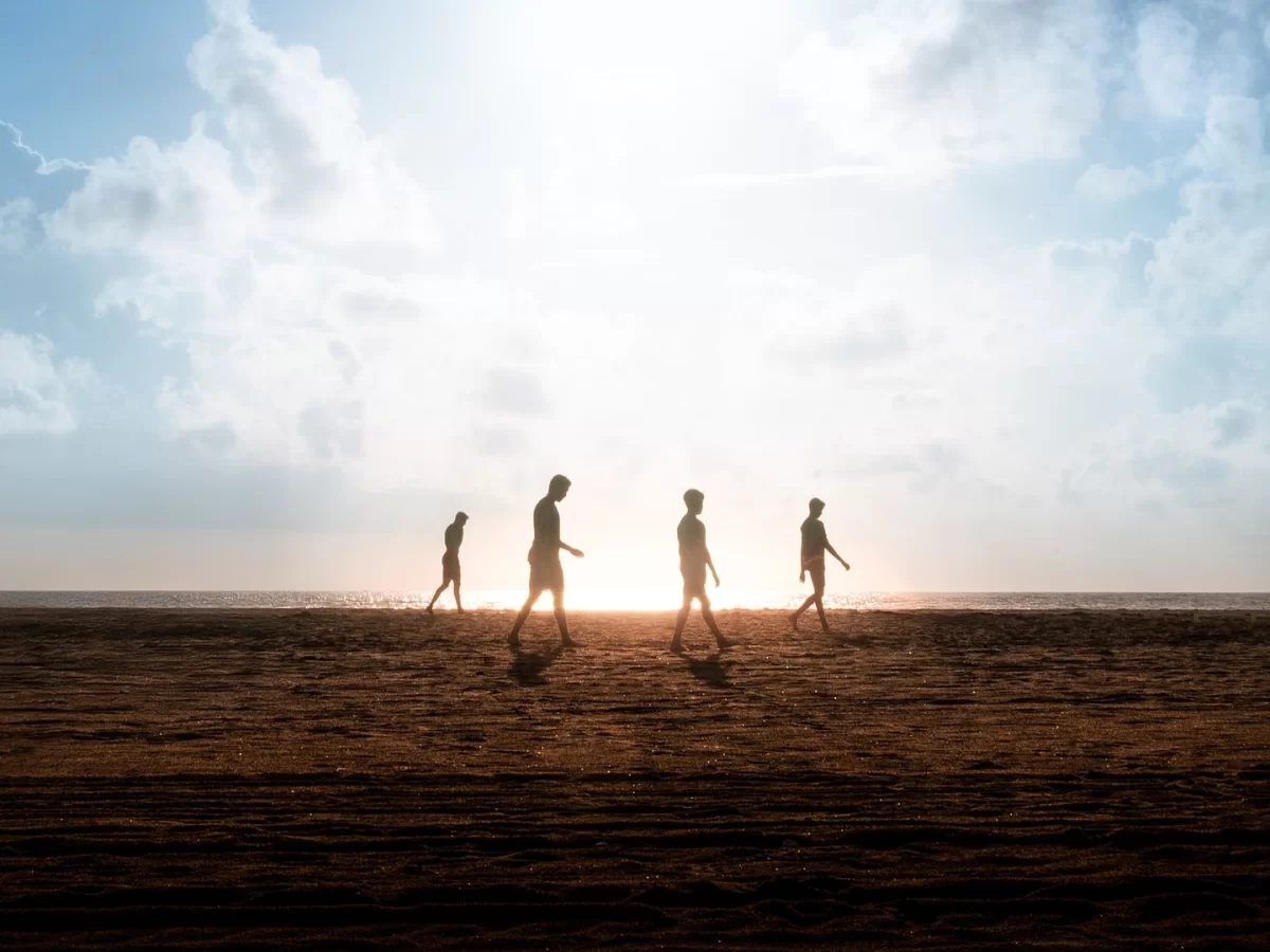 Silhouettes of friends walking on Marina Beach Chennai during sunset, featuring sandy shore, glowing sun rays, partly cloudy sky, perfect romantic beach experience Chennai tour package.