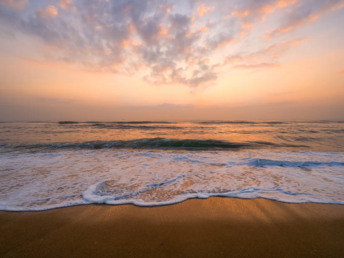 Besant Nagar Beach during vibrant sunset, featuring orange-pink skies, gentle waves, golden sands reflections, perfect romantic coastal experience with Chennai beach tour package.