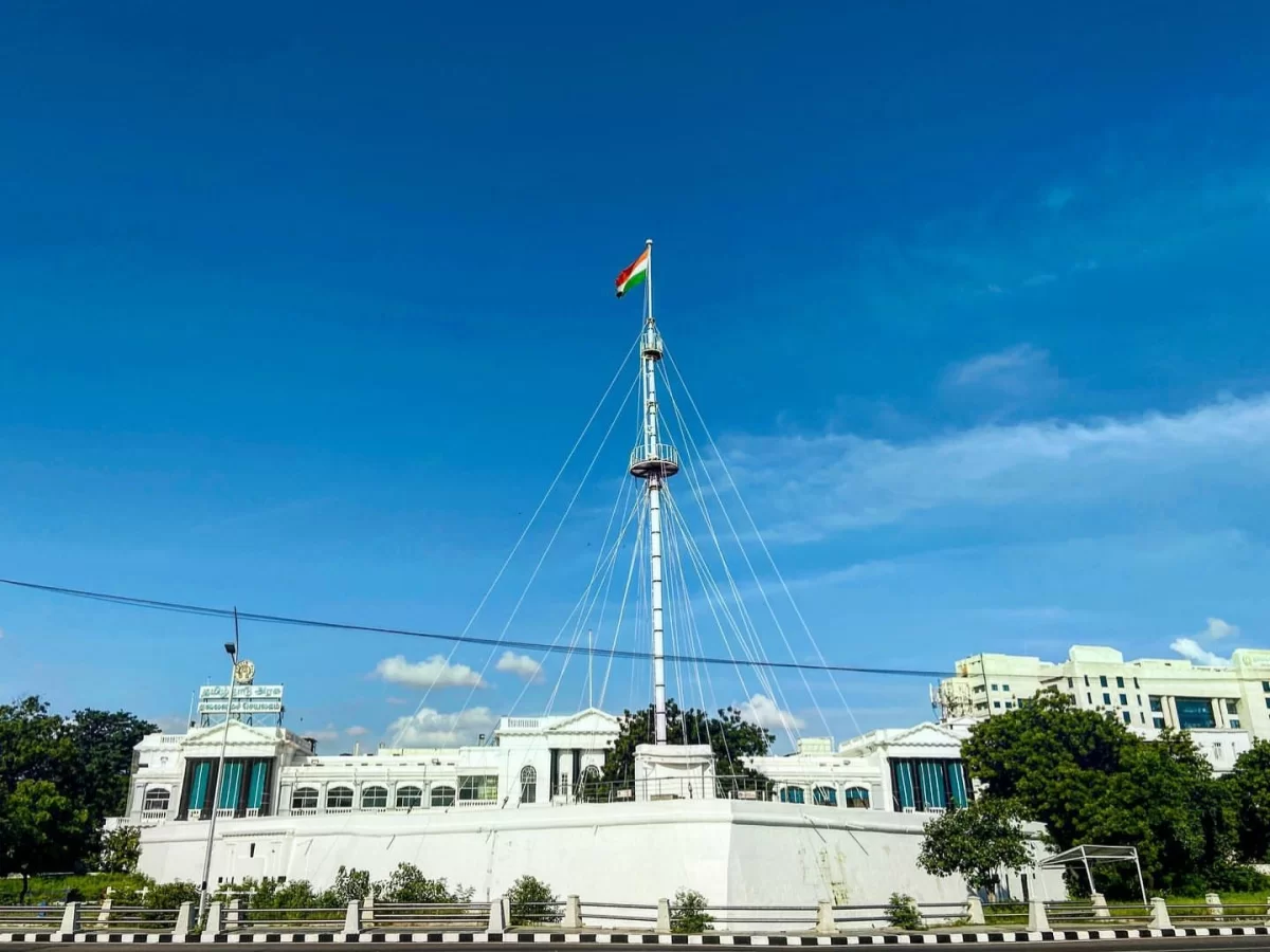 Fort St. George Museum Chennai during clear blue sky day, featuring white colonial structure Indian flag flagstaff, green lawns trees, perfect historical museum experience Chennai tour package.