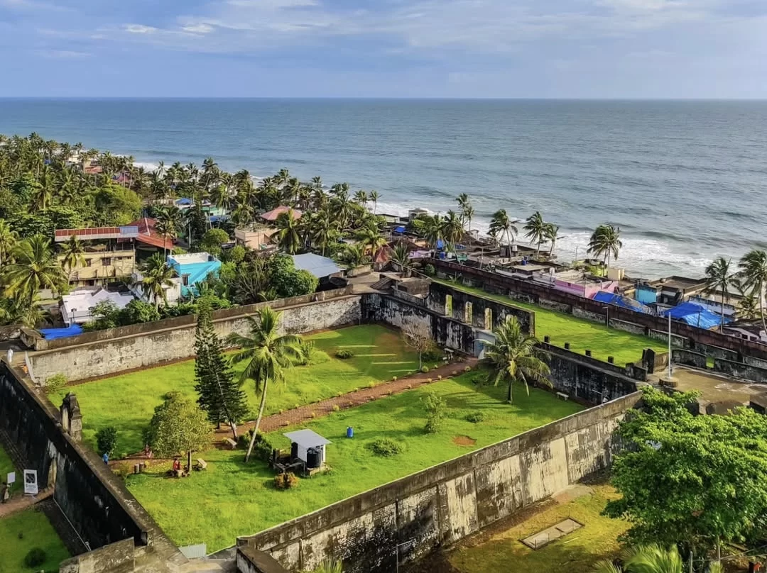 Stunning aerial view of Anjuthengu Fort Kerala showcasing walled courtyard with palms against vast Arabian Sea, surrounded by colorful village homes, perfect historical coastal adventure with Varkala tour package. 