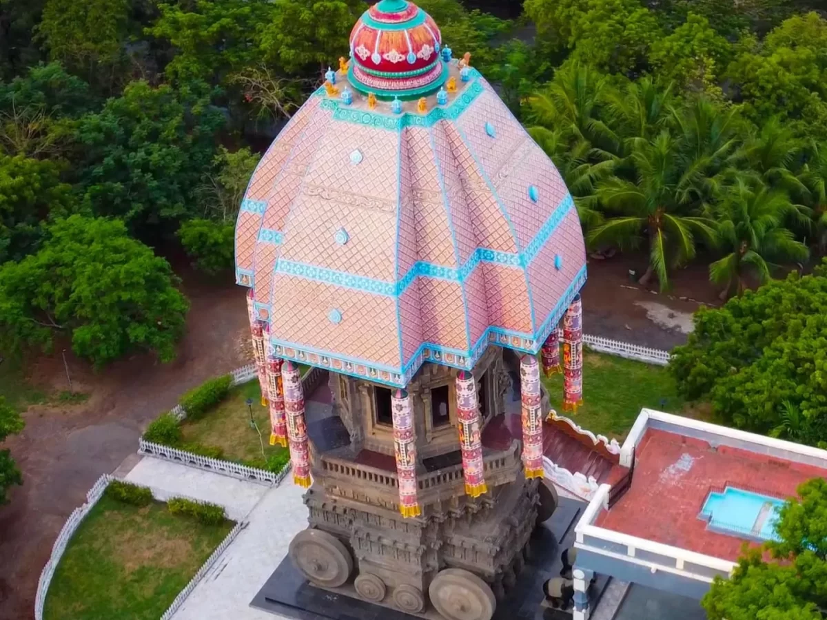 Aerial daytime Valluvar Kottam Chennai stone chariot replica lush greenery palms, featuring ornate pink terracotta dome hanging decorations wheels pillars, perfect Thiruvalluvar memorial Chennai tour package.