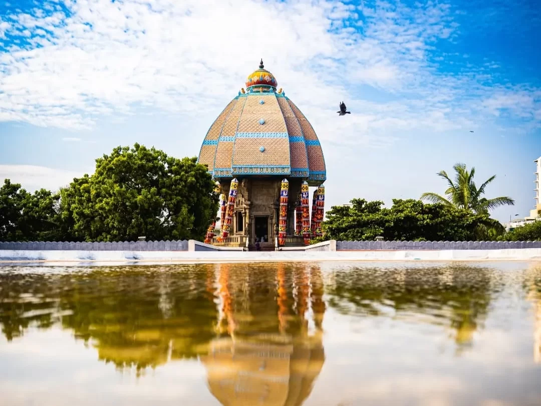 Reflective pond foreground Valluvar Kottam Chennai chariot dome trees palms blue sky bird flying, featuring ornate terracotta Thiruvalluvar memorial symmetrical mirror image, perfect iconic cultural Chennai tour package