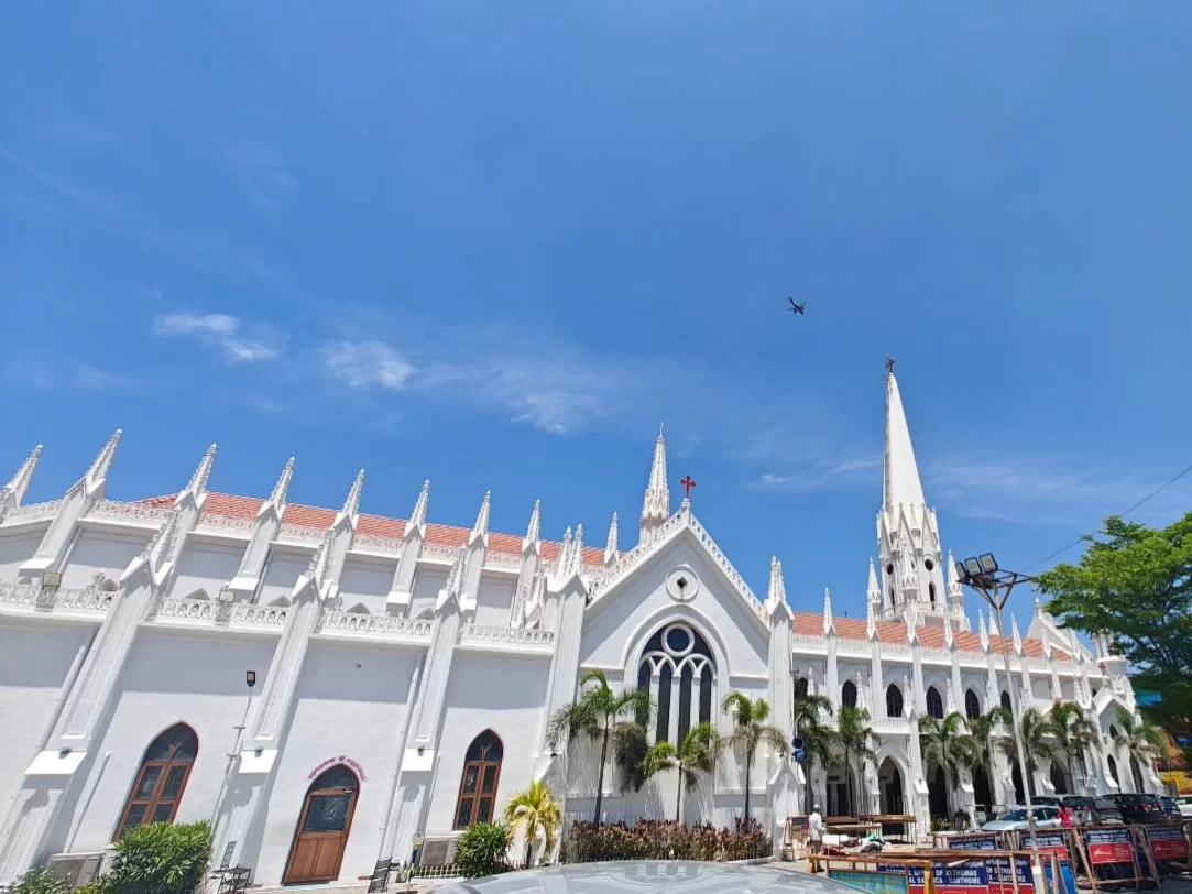 Santhome Cathedral Basilica Chennai during clear sunny day, featuring white Gothic spires, red roofs, palm trees, arched windows, perfect spiritual heritage experience Chennai tour package.