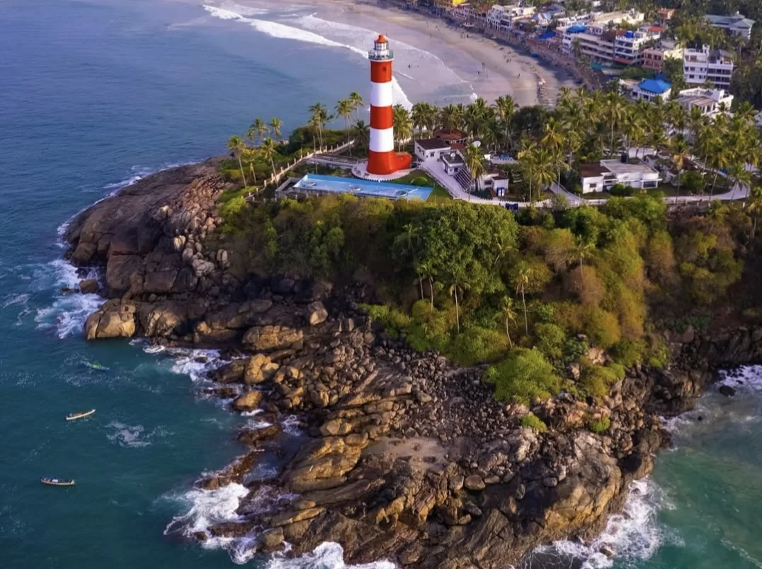 Kovalam Lighthouse Beach Kerala drone aerial view rocky outcrop brown stones ocean turquoise waves crashing white foam coastal scenic landmark tourism photography dramatic sea surf high tide. 