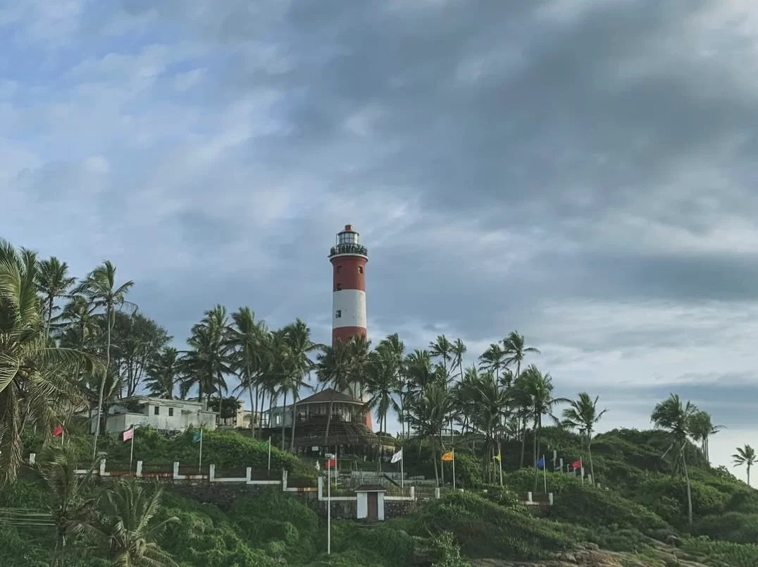 Kovalam Lighthouse Beach Kerala drone aerial view brown rocky outcrop ocean turquoise waves crashing white foam coastal scenic landmark tourism photography high tide surf dramatic sea texture. 