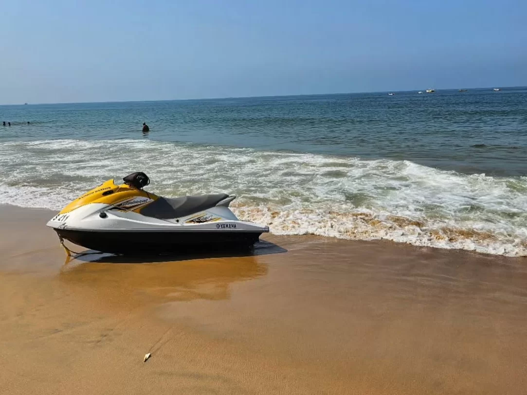 Yellow white jet ski parked on sandy shore at Candolim Beach Goa during sunny day, featuring gentle Arabian Sea waves distant swimmers boats horizon, perfect water sports adventure experience with Candolim Beach Goa tour package.