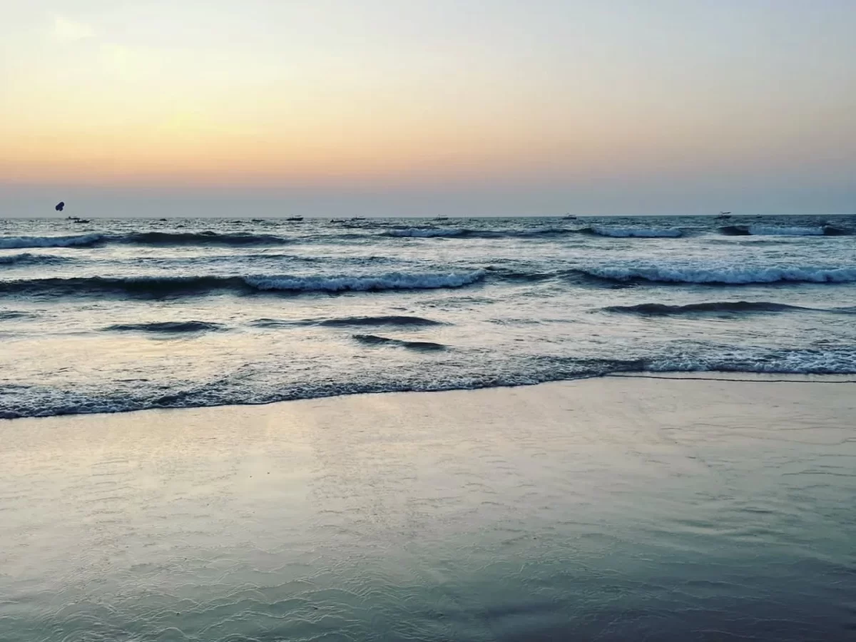 Sunset view of crashing waves at Candolim Beach Goa during golden hour evening, featuring orange sky distant sailboats Arabian Sea horizon, perfect romantic beach experience with Candolim Beach Goa tour package. 