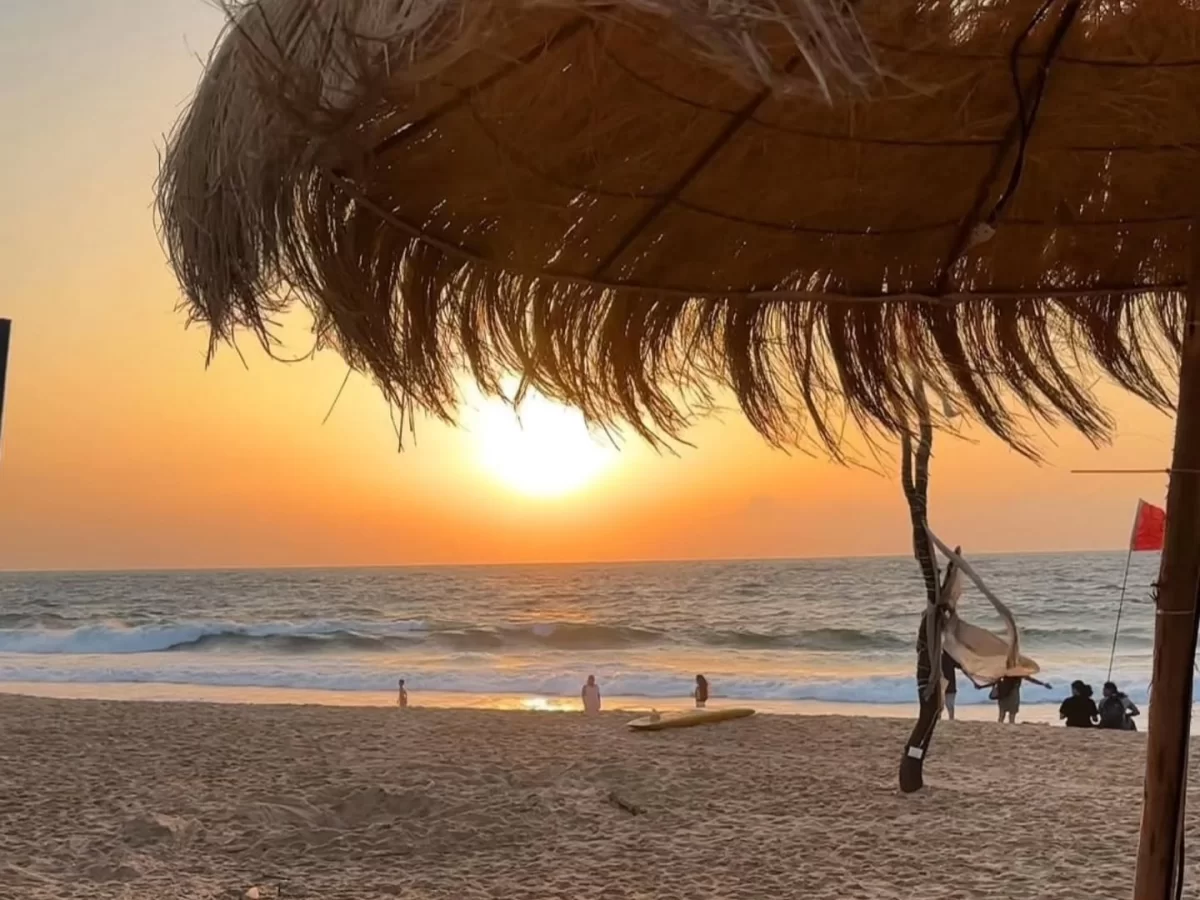 Thatched beach umbrella at Calangute Beach Goa during sunset, featuring golden sun surfers Arabian Sea waves, perfect romantic experience with Calangute Beach Goa tour package. 