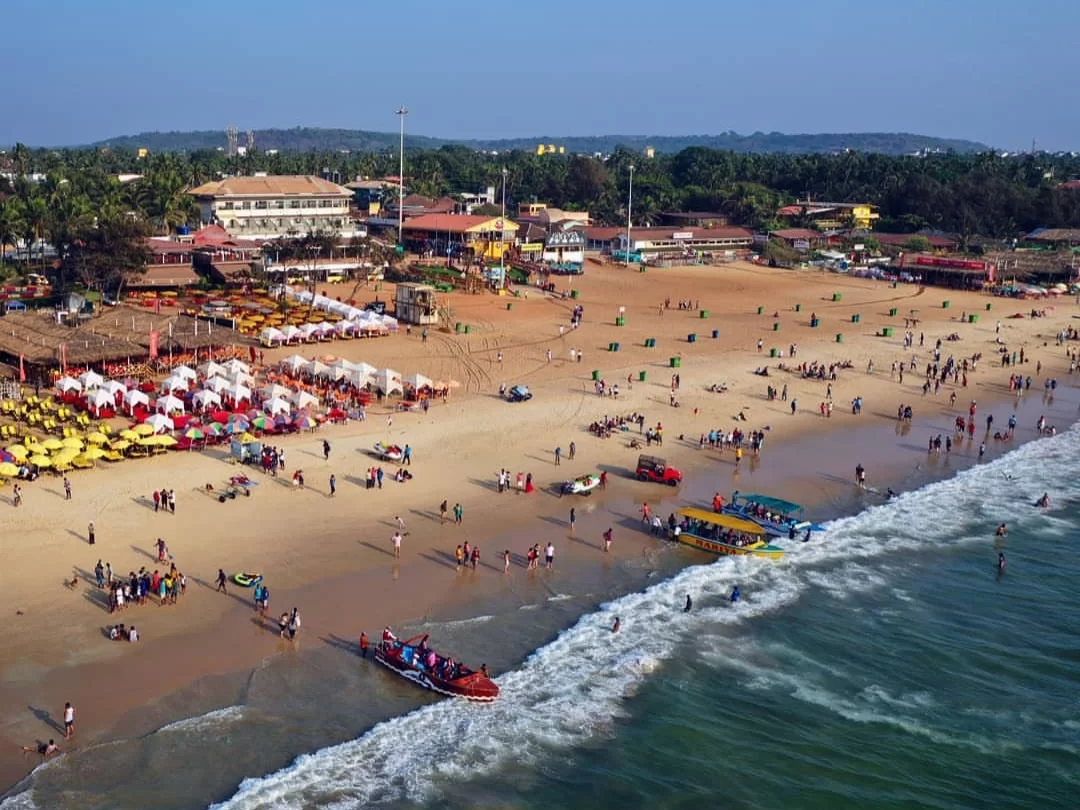 Aerial view of vibrant Calangute Beach Goa during sunny day, featuring colorful umbrellas shack crowds boats Arabian Sea waves, perfect beach adventure experience with Calangute Beach Goa tour package.