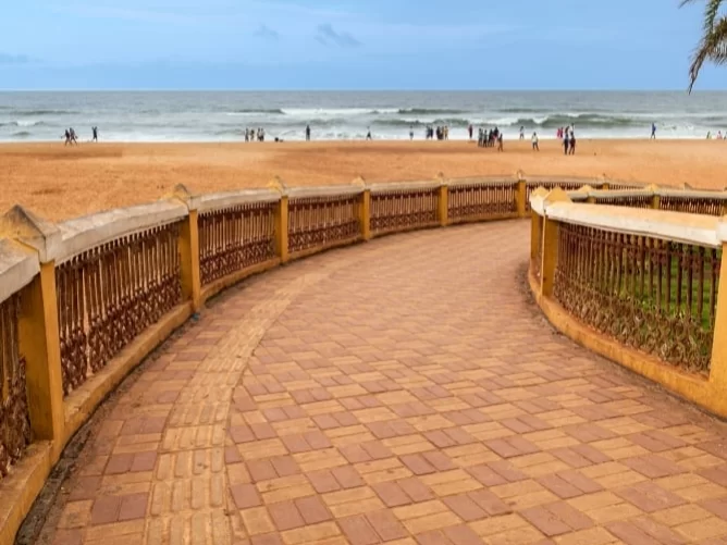 Curved promenade railing at Calangute Beach Goa during partly cloudy day, featuring sandy shore distant Arabian Sea waves palm trees, perfect beach walk experience with Calangute Beach Goa tour package.