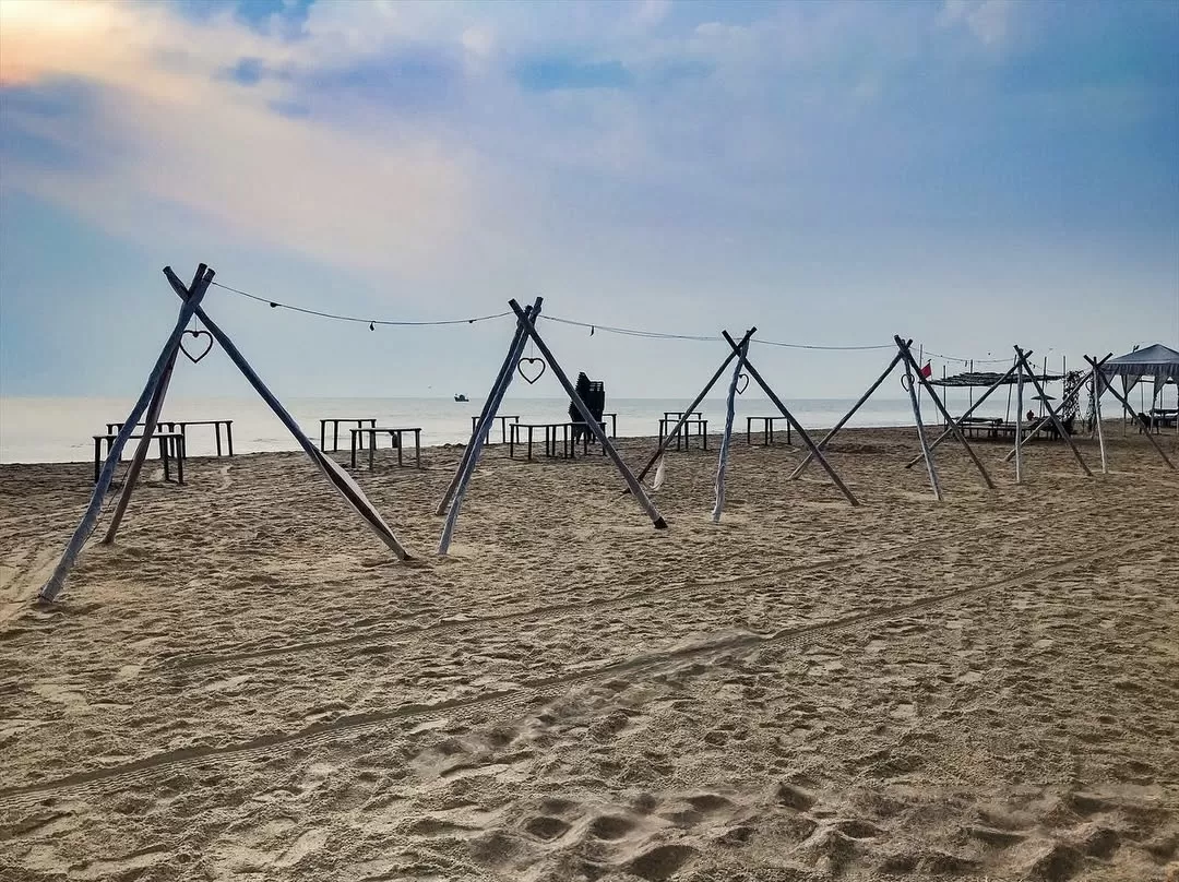Heart-shaped bamboo frames with fairy lights Betalbatim Beach Goa twilight, featuring beach chairs tents silhouetted sea sandy expanse, perfect South Goa beach tour package.