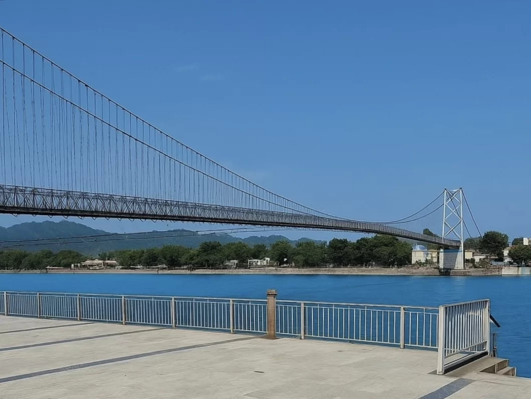 Laxman Jhula suspension bridge at Rishikesh over Ganga River, featuring steel cables towers blue water distant mountains riverside railing, perfect spiritual experience Uttarakhand tour package.