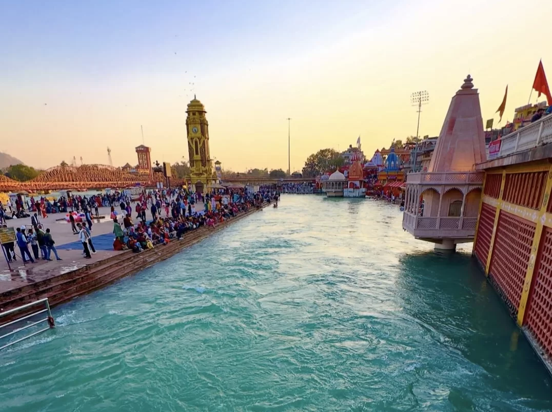 Har Ki Pauri Haridwar golden hour Ganga ghats with yellow clock tower colorful temples tents devotees bridge reflections, perfect spiritual riverside aarti, Uttarakhand tour packages.