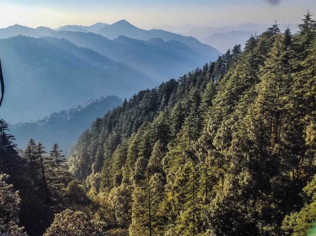 Kempty Falls panoramic sunrise layered misty blue mountains dense green deodar pine forests valley view golden sunlight rays backdrop, perfect scenic viewpoint Mussoorie area Uttarakhand tour packages.