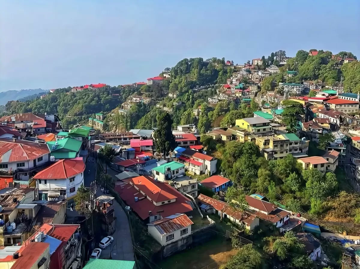 Landour village panoramic view during sunny day, featuring colorful hillside houses and green hills, perfect adventure Uttarakhand tour package.