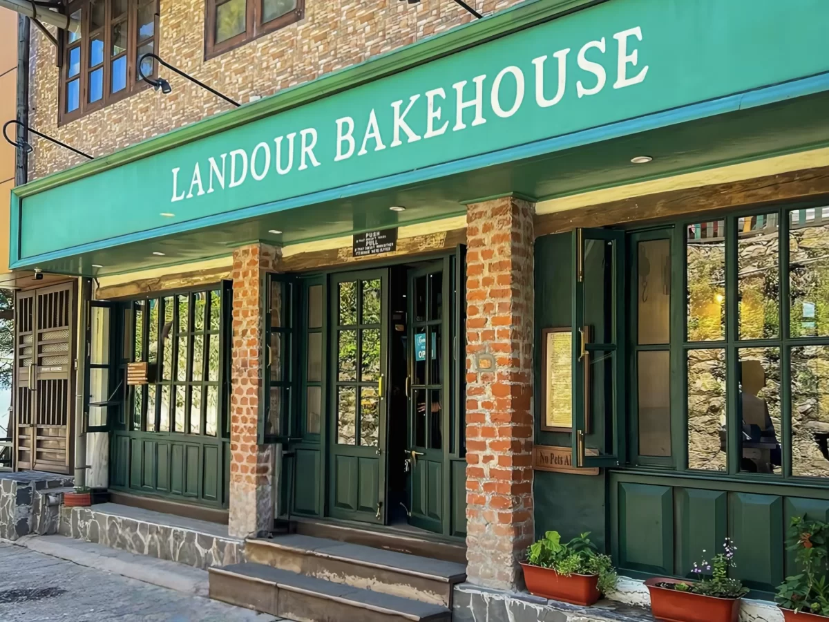 Landour Bakehouse at Landour during sunny day, featuring green facade, brick walls and potted plants, perfect adventure Uttarakhand tour package.
