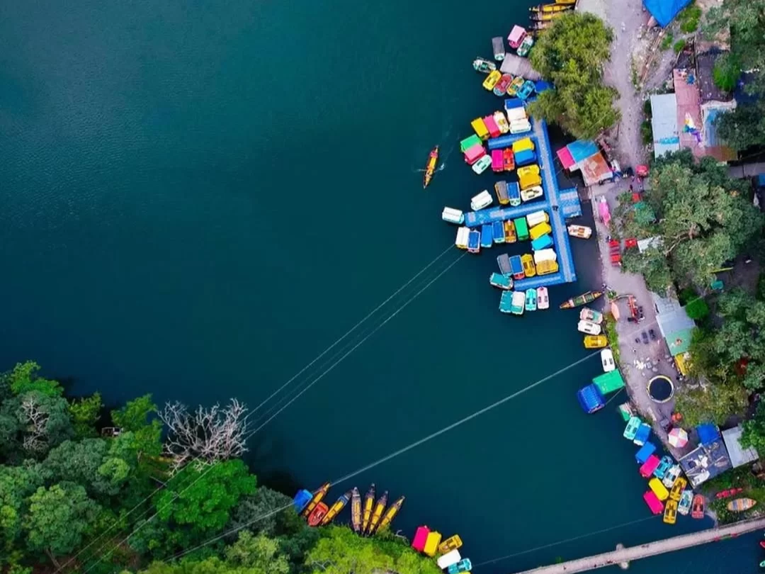 Aerial view of colorful boats docked at Sattal Lake Nainital during daytime, featuring vibrant kayaks and green hills, perfect adventure experience Uttarakhand tour package.