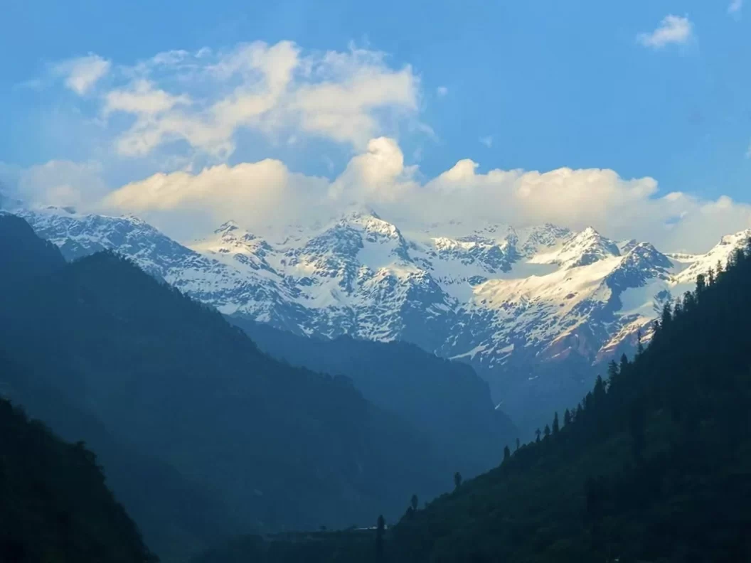 Snow-capped Himalayan peaks at Gangotri valley during clear evening sky, featuring deep green forests, perfect adventure experience Uttarakhand tour package.