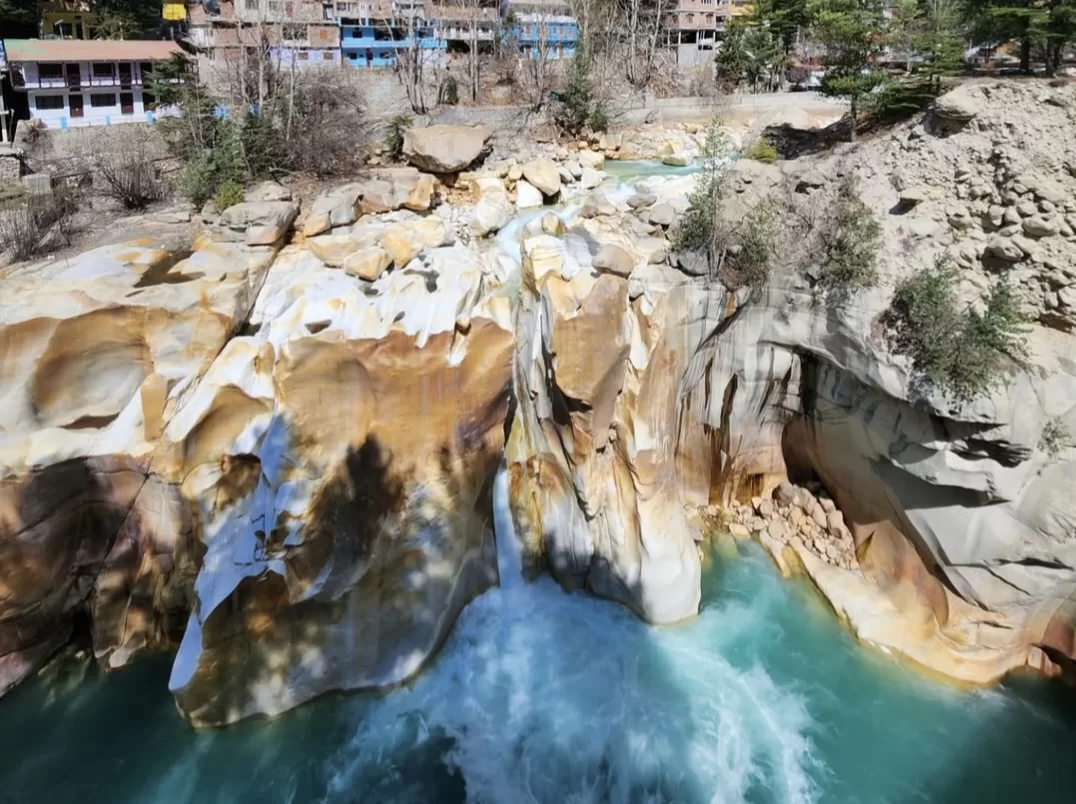 Turquoise Bhagirathi river waterfall at Surya Kund near Gangotri Temple in Uttarakhand during sunny day, featuring carved rocks, perfect adventure Uttarakhand tour package.