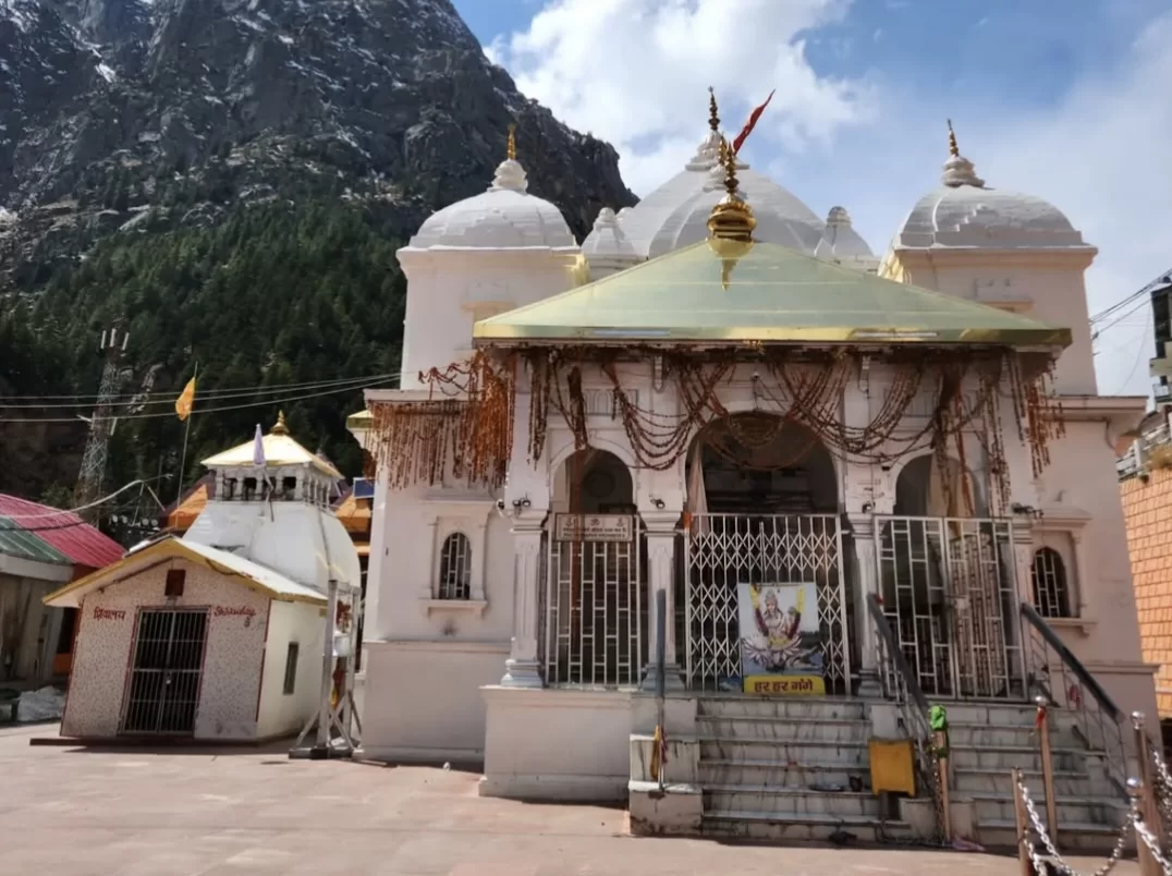 Devotees at Gangotri Temple in Uttarkashi during sunny day, featuring white Nagara-style shrine and Himalayan mountain backdrop, perfect spiritual Uttarakhand tour package.