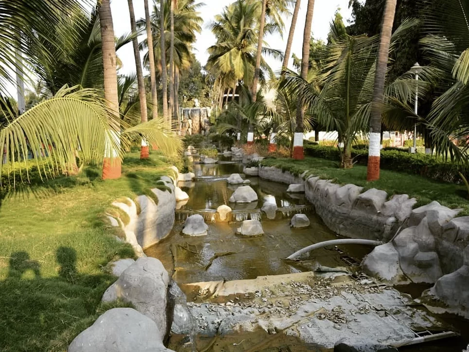 Scenic walkway at Siddharth Garden and Zoo Aurangabad during sunny day, featuring palm avenue, artificial stream, red-white planters, perfect relaxation experience with Aurangabad family tour package. 
