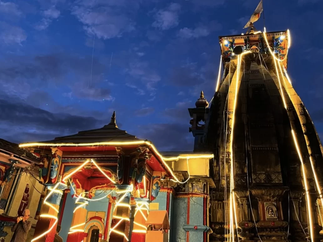 Ukhimath Omkareshwar Temple night illuminated towering shikhara colorful temple facade lights strings blue starry sky clouds flags, perfect festive Shiva Kedarnath winter shrine, Uttarakhand tour packages.