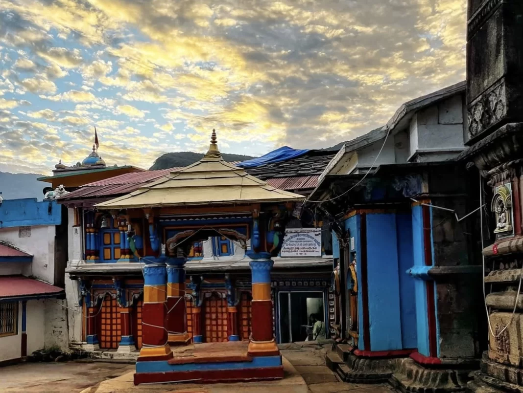 Ukhimath Omkareshwar Temple golden sunset clouds colorful pagoda temple intricate blue yellow red carvings pillars distant mountains, perfect Shiva winter abode Kedarnath dham, Uttarakhand tour packages.