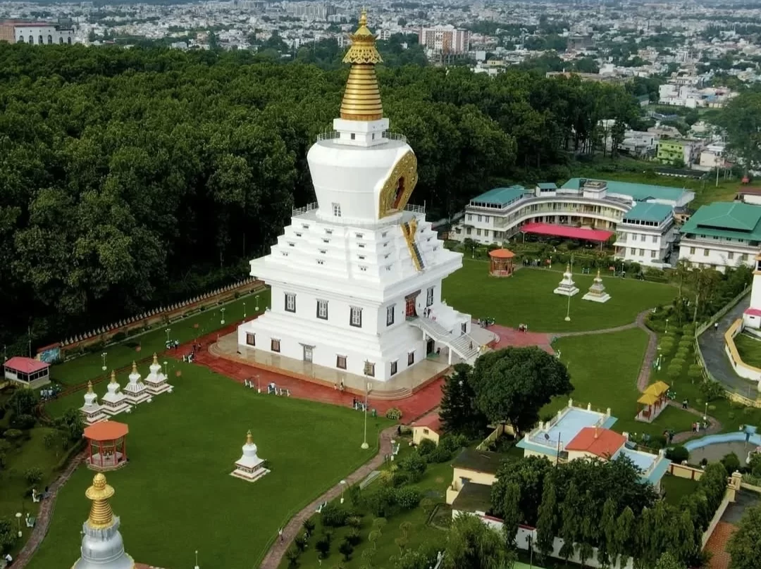 Tibetan stupa at Mindrolling Monastery Clement Town during sunny day, featuring white-gold tower surrounded by green lawns and Dehradun cityscape, perfect spiritual experience Uttarakhand tour package.