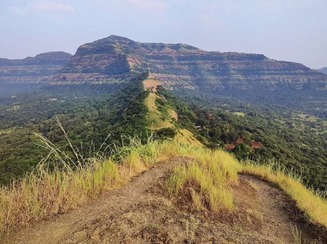 Trek path to Visapur Fort summit during hazy day, featuring basalt cliffs & Sahyadri forests, perfect adventure experience Maharashtra tour packages.