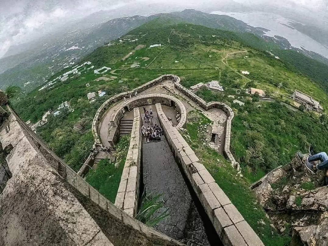 Aerial view of Visapur Fort during misty day, featuring stone ramparts & Lonavala valley lake, perfect adventure experience Maharashtra tour packages. 