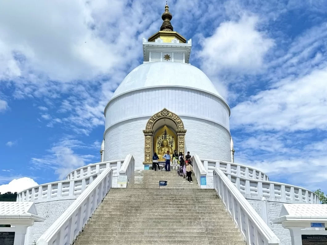 Peace Pagoda Darjeeling during partly cloudy day West Bengal, featuring white stupa golden Buddha entrance tourists wide stone stairs blue sky hills backdrop, perfect West Bengal tour packages.