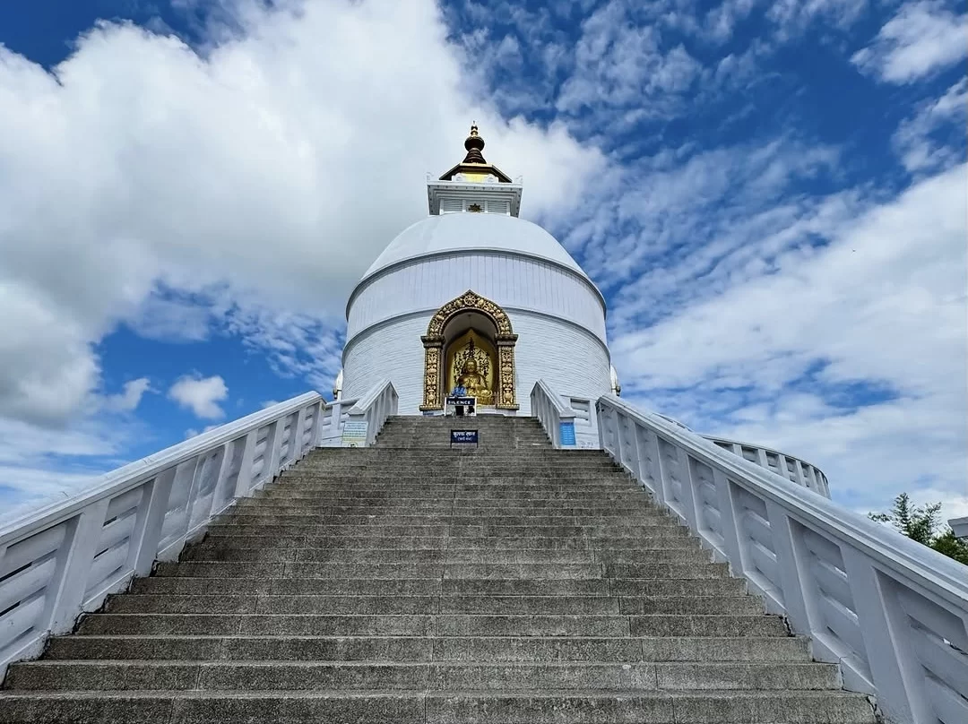 Peace Pagoda Darjeeling during partly cloudy day West Bengal, featuring white stupa golden Buddha entrance wide stone stairs blue sky hills backdrop, perfect West Bengal tour packages.