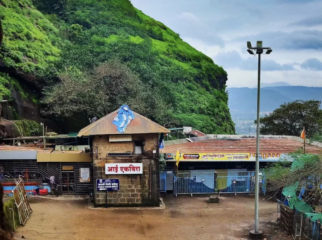 Aadishakti Aai Ekvira Devi Temple entrance gate amid lush green Sahyadri hills near Karla Caves Lonavala, featuring Marathi signboard and saffron flags, perfect adventurous pilgrimage trek with Maharashtra tour package. 