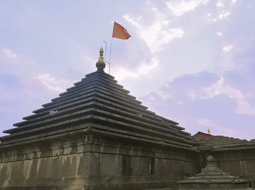 Mahabaleshwar Temple shikhara during partly cloudy day Maharashtra, featuring tiered basalt stone spire saffron flag gold kalash adjacent shrines blue sky backdrop, perfect Maharashtra tour packages.