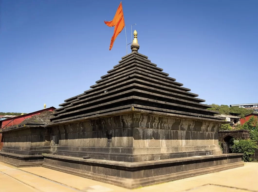 Mahabaleshwar Temple shikhara during sunny day Maharashtra, featuring tiered basalt stone spire saffron flag gold kalash blue sky hill backdrop, perfect Maharashtra tour packages. 
