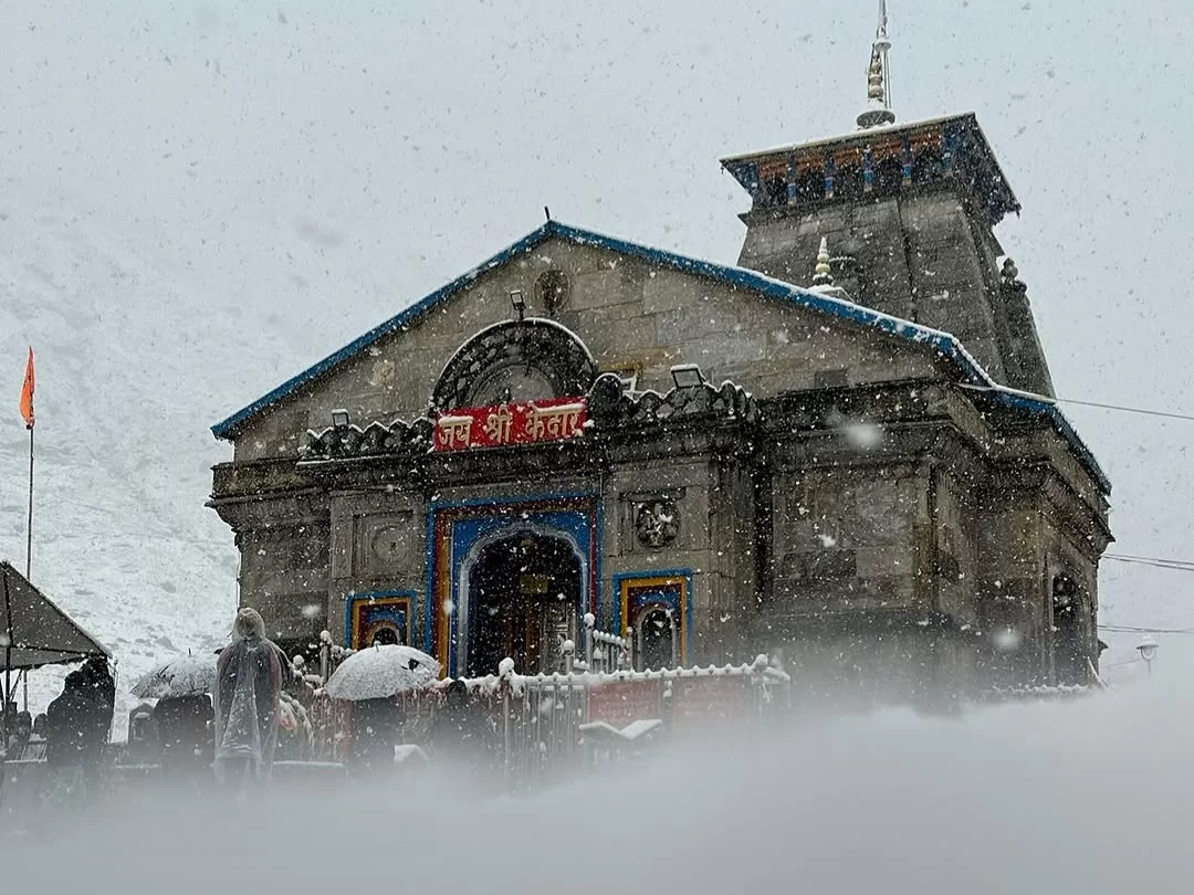Kedarnath Temple during heavy snowfall, featuring snowy facade, devotees and Himalayan peaks, perfect spiritual Kedarnath tour package.