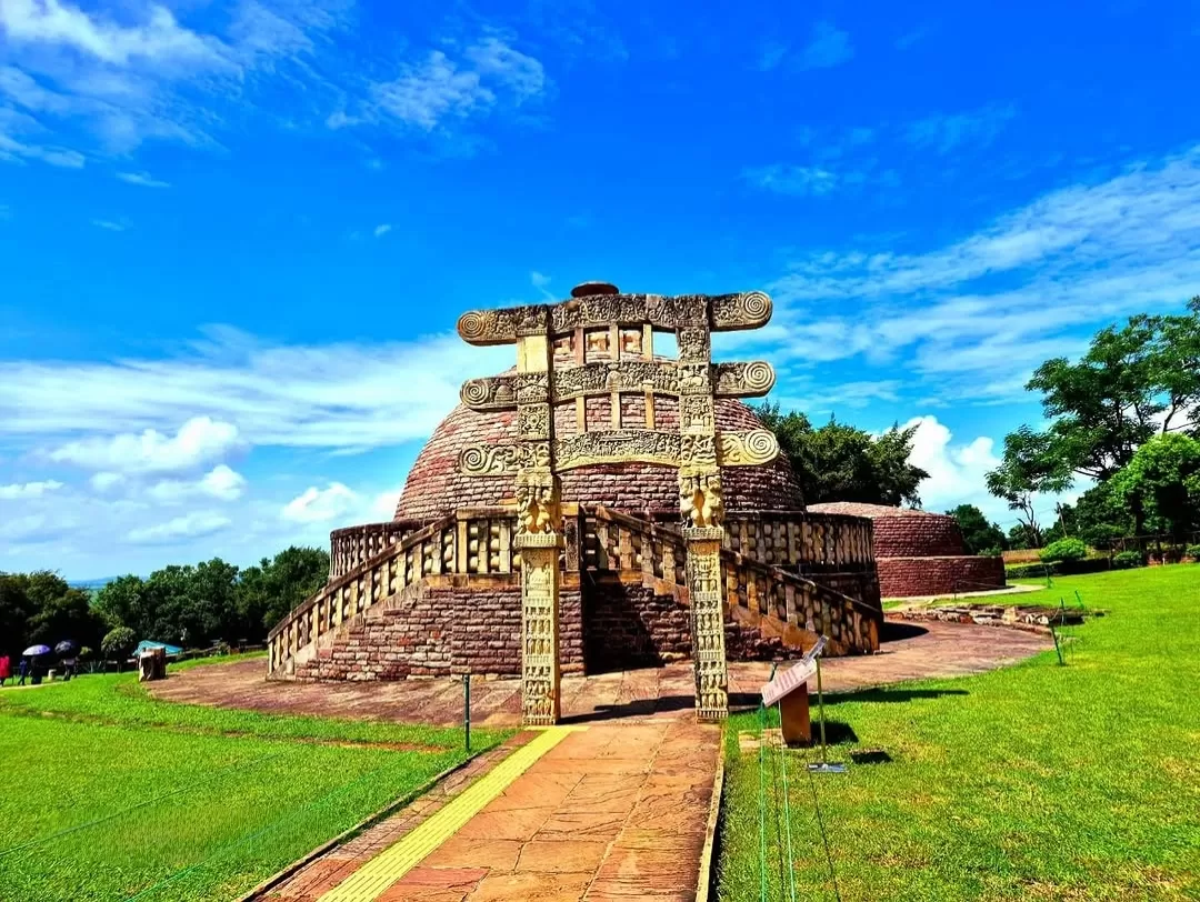 Great Stupa at Sanchi during clear afternoon, featuring ornate Torana gateway with carvings and lush green surroundings, perfect heritage experience in Madhya Pradesh tour package.