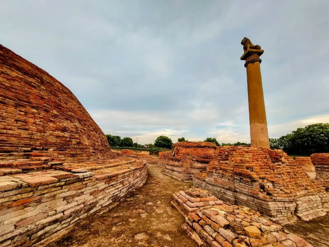 Ashoka Pillar with horse capital at Sanchi during golden sunset, featuring ancient stupa ruins and brick foundations, perfect heritage experience in Madhya Pradesh tour package.