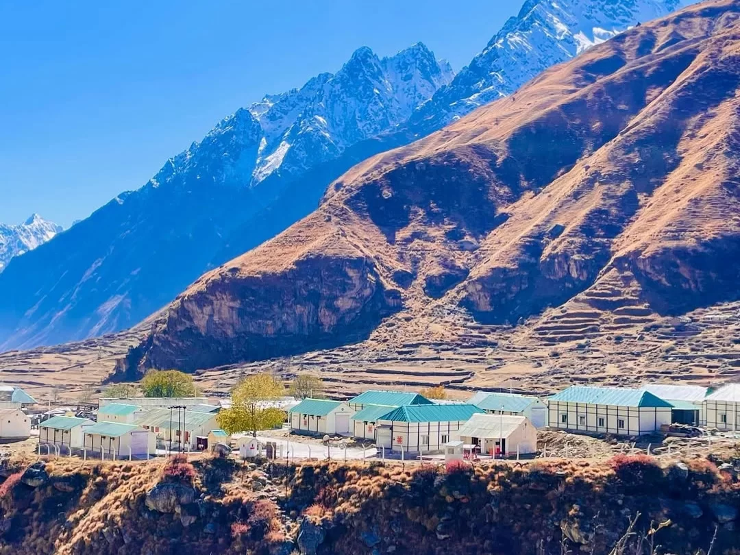Mana Village Uttarakhand green roof houses terraced fields snowy Himalayan peaks blue sky clouds Badrinath last Indian village Uttarakhand tour packages. 