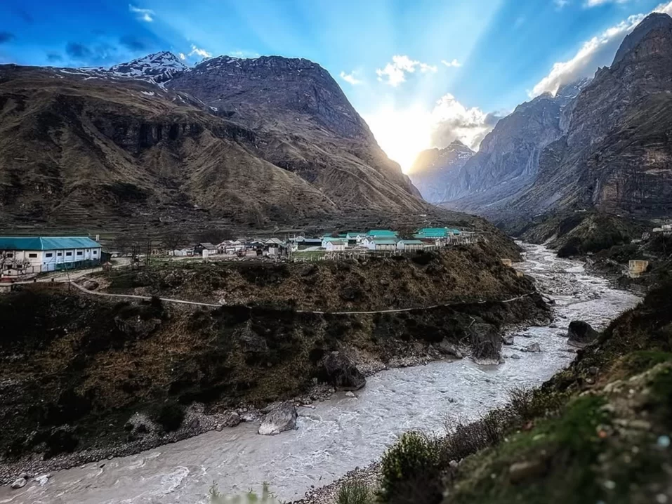 Mana Village Uttarakhand green roof houses white buildings snowy Himalayan peaks river valley golden hour sunlight Badrinath Char Dham Uttarakhand tour packages.