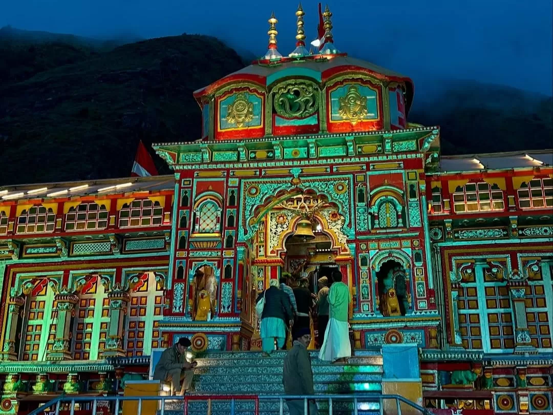 Colorful illuminated Badrinath Temple Uttarakhand at night during misty weather, featuring ornate facade and Himalayan backdrop, perfect spiritual experience Uttarakhand tour packages.