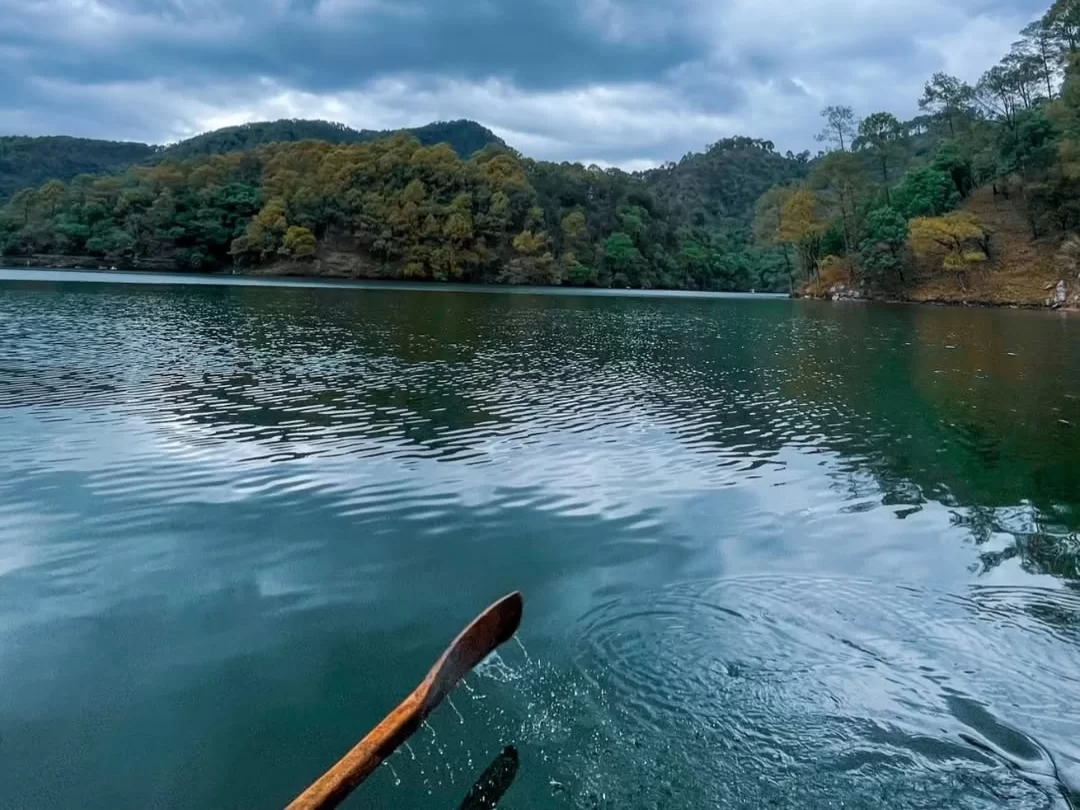 Rowboat paddling at Sattal Lake Nainital during cloudy afternoon, featuring emerald waters and oak-covered hills, perfect adventure experience Uttarakhand tour package.