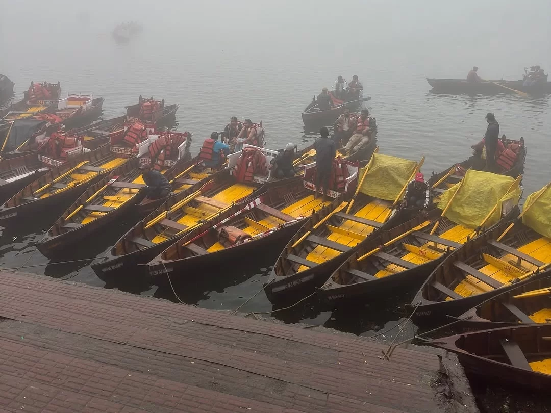 Rowboats docked at Naukuchiatal Lake Nainital during misty foggy morning, featuring yellow canopies and distant hills, perfect adventure experience Uttarakhand tour package.